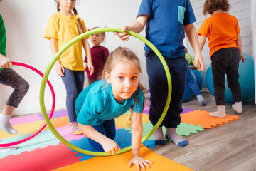 Curly girl crawling on colorful floor through hula hoops © oksix