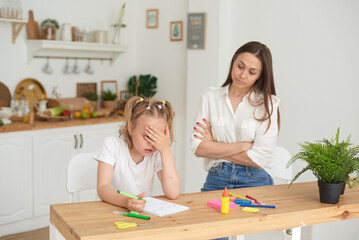 Obraz na płótnie Canvas Young girl doing homework during extra-curricular classes with a tutor. Frustrated young mother or tutor teaching kid at home, remote school education. A worried young parent scolds his child. Quarrel