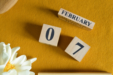 February 7, Wooden Calendar cube on yellow felt fabric with peony flower for date icon background.