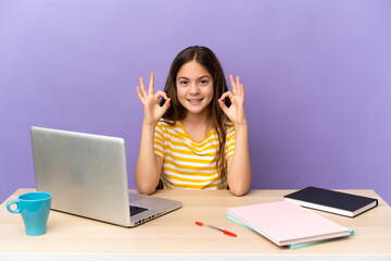 Little student girl in a workplace with a laptop isolated on purple background showing ok sign with two hands