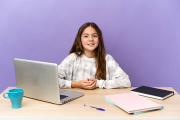 Little student girl in a workplace with a laptop isolated on purple background laughing