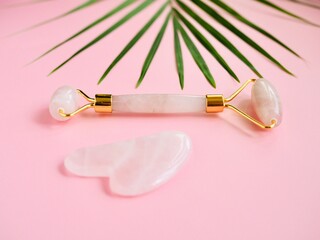 Rose quartz jade face roller. Pink Gua Sha massage tool on pink background. Facial skin care and body treatment at home, anti-aging, anti-wrinkle and lifting therapy. SPA beauty treatment, relaxation