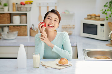 Smiling happy woman eating fresh apple for breakfast while sitting in a kitchen