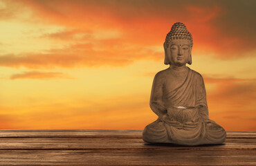 Beautiful stone Buddha sculpture on wooden surface at sunset. Space for text