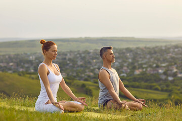 Man and woman meditating in Lotus pose. Middle aged yogi couple sitting cross legged and breathing fresh air enjoying peace and quiet of nature. Yoga trainer and student relaxing in Padmasana