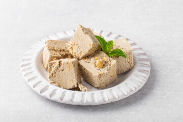 pieces of sunflower halva with peanuts in a gray plate, mint, light gray background, oriental sweets