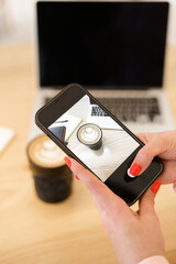 Woman hand taking picture of coffee and laptop on the table. Blogger taking lifestyle photo for social media. Black laptop screen