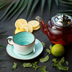Full teapot with lemon and mint Black tea and empty cup on dark table background. Lime, lemon...