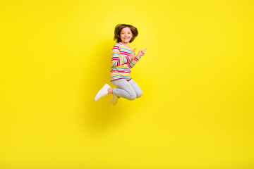 Fototapeta na wymiar Full body photo of charming cheerful young small girl jump up point finger empty space isolated on yellow color background