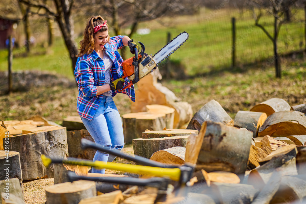 Wall mural Young Woman using chainsaw to cut a log for firewood.