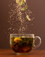 Herbal vitamin tea. Ingredients falling into glass cup with drink. Close up shot in motion on brown background. Side view. Soft focus.