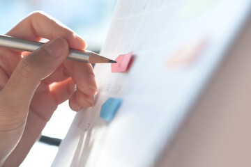 Woman hand with a pencil taking note on work planner schedule on desktop calendar, checking...