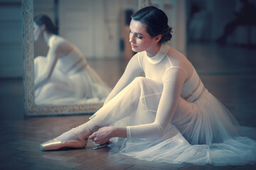 Beautiful ballerina is tying pointe shoes. Image with selective focus, noise effect and toning - obrazy, fototapety, plakaty