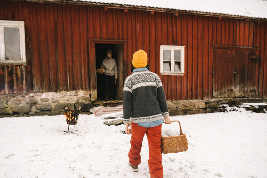 Kvinna med korg g&aring;r mot stuga under vintern