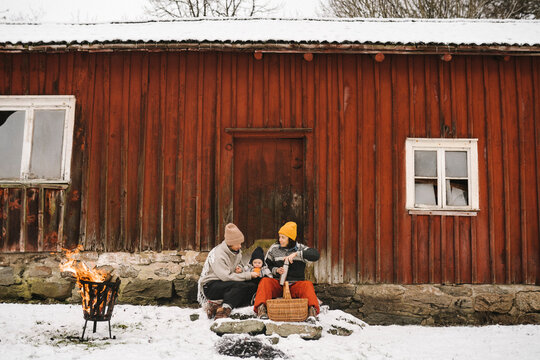 Mammor med barn sittande utanf&ouml;r stuga i sn&ouml;n