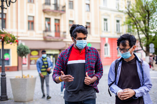 Two young multiracial friends in masks chatting outdoors