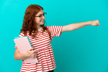 Student teenager redhead girl isolated on blue background giving a thumbs up gesture