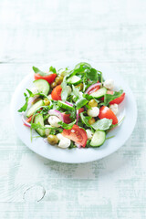 Summer Salad with Mozzarella Cheese, Cucumber, green Olives, Tomatoes and fresh Rocket. Bright wooden background. Copy space. 
