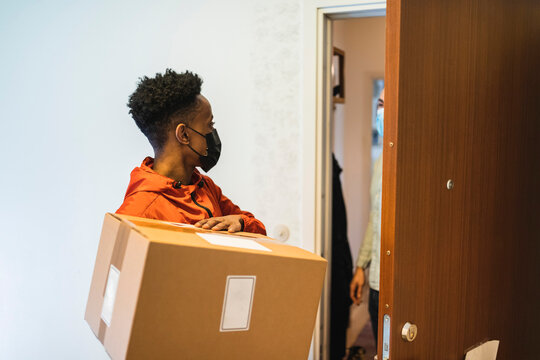 Manligt bud med paket st&aring;r utanf&ouml;r ytterd&ouml;rr i trapphus
