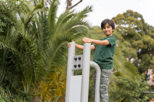 Young boy on gym equipment outdoors. Smart Indian child climbed on top of gym equipment.