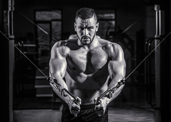 Fototapeta na wymiar Fitness man execute exercise with exercise-machine Cable Crossover in gym. Handsome man with big muscles in gym. Machine in the gym. Black and white
