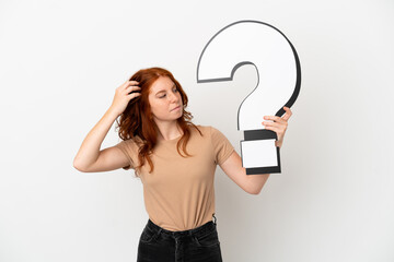 Teenager redhead girl isolated on white background holding a question mark icon and having doubts