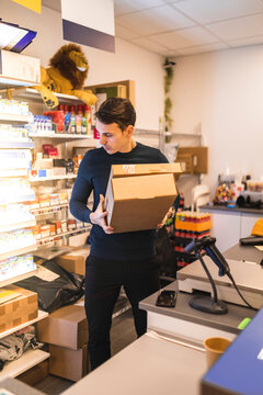 Butiks&auml;gare st&aring;r bakom kassa och h&aring;ller paket