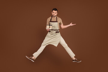 Fototapeta na wymiar Full length body size man wearing apron jumping up keeping coffee unhappy dissatisfied isolated brown color background