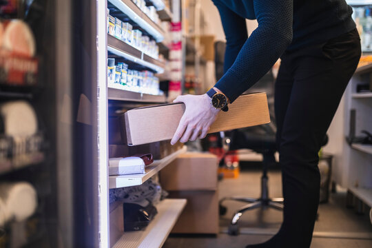 Butiks&auml;gare l&auml;gger in paket i hylla bakom kassa