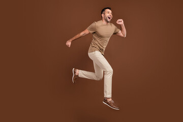 Fototapeta na wymiar Full length body size man in casual outfit running jumping up overjoyed isolated brown color background