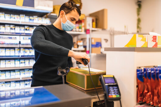 Manlig butiks&auml;gare skannar paket st&aring;ende bakom kassa