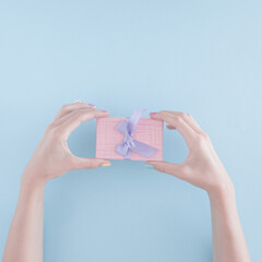 a woman's hand with a present box on pastel blue background. abstract art. minimal creative decoration idea