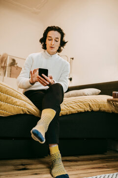 Man anv&auml;nder smartphone sittande p&aring; s&auml;ng i sovrum