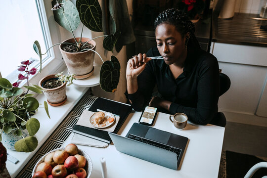 Fundersam kvinna sitter vid dator och arbetar hemifr&aring;n