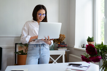 Image of young cheery positive beautiful business woman sitting indoors in office or home office using laptop computer.