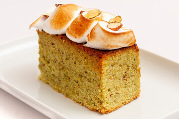 Cake slice with pistachio and white meringue on white plate