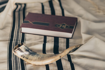 A shofar is placed on a tallit next to a close Torah study book. Before the Jewish holidays on the...