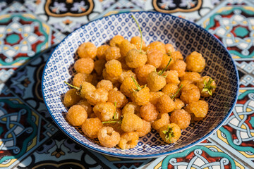 Blue plate full of fresh yellow raspberries on garden table.
