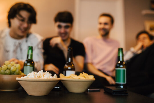 Manliga v&auml;nner sitter i vardagsrum med snacks och &ouml;l hemma