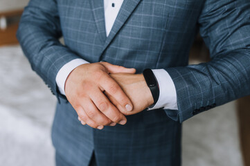 A man, a businessman, a director in a blue plaid suit, holds his arms crossed and looks at a black smart watch. Photography, concept. Portrait of a man.