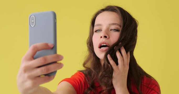 Beautiful woman talking selfie on mobile phone over yellow background
