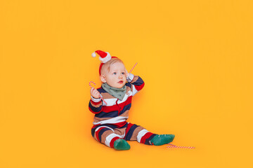 Little boy in claus hat holding candy in his hands in front of yellow background