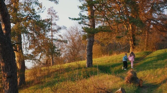 Friends having scamper in the forest. Young guy and girl are running in the morning in nature. Young people run at sunset. Rear view.