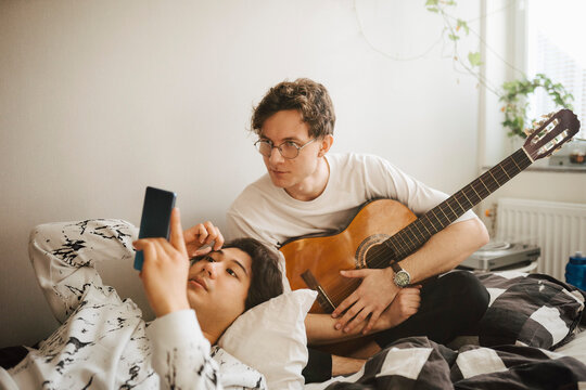 Man med gitarr tittar p&aring; kompis smartphone hemma