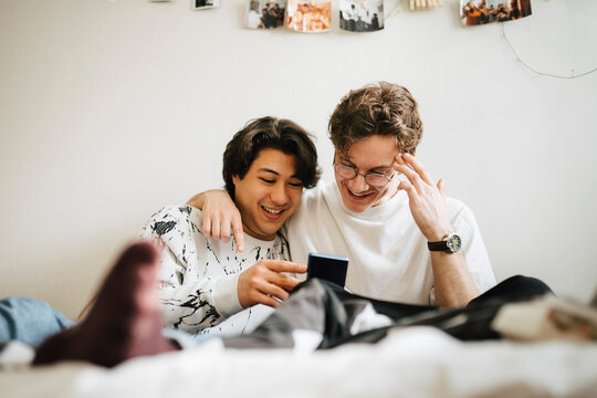 Glada v&auml;nner sitter i sovrum och anv&auml;nder smartphone