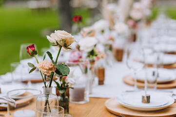 Beautiful multi-colored roses stand in a glass vase against the background of a wooden table with dishes at a banquet. Photography, concept.