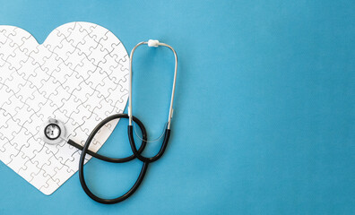White puzzle in heart shape and stethoscope on blue background. Heart health concept