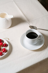  Coffee, milk and sweet cherries on linen tablecloth, breakfast