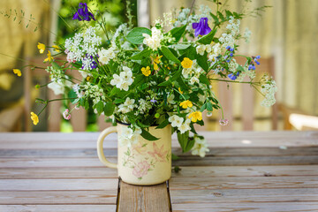 Bouquet of field flowers in old mug standing on a garden table 