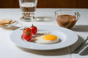 Fried egg with tomatoes on white plate, breakfast dining table